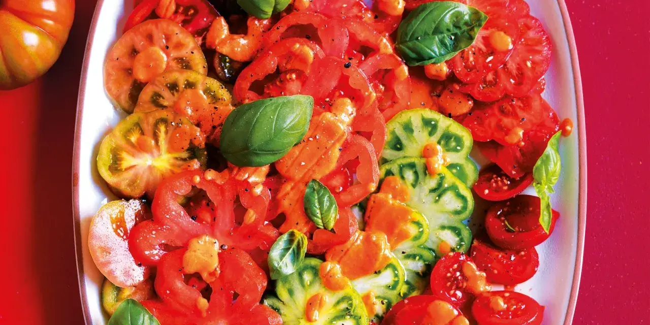 Un colorato carpaccio di pomodoro, con fette di diverse varietà, condito con olio e basilico fresco.