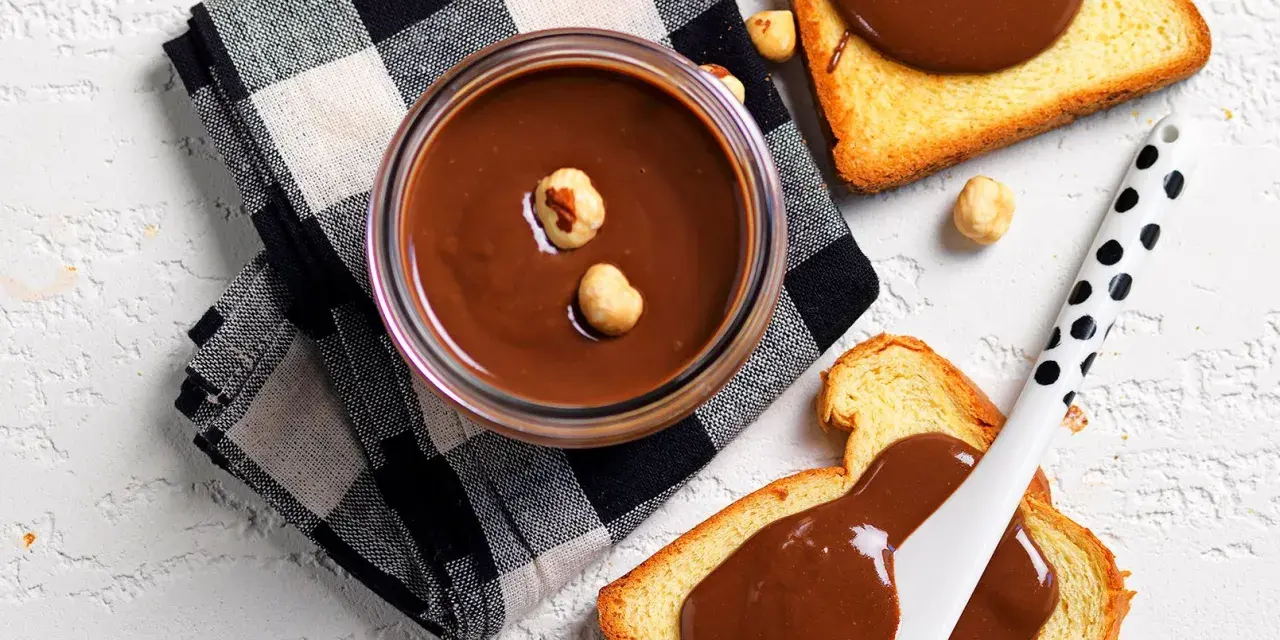 Crema di nocciole fatta in casa in un barattolo, con fette biscottate e nocciole sparse.