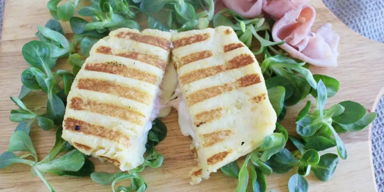Toast di patate grigliato, ripieno di prosciutto e formaggio filante, servito su un letto di insalata fresca.