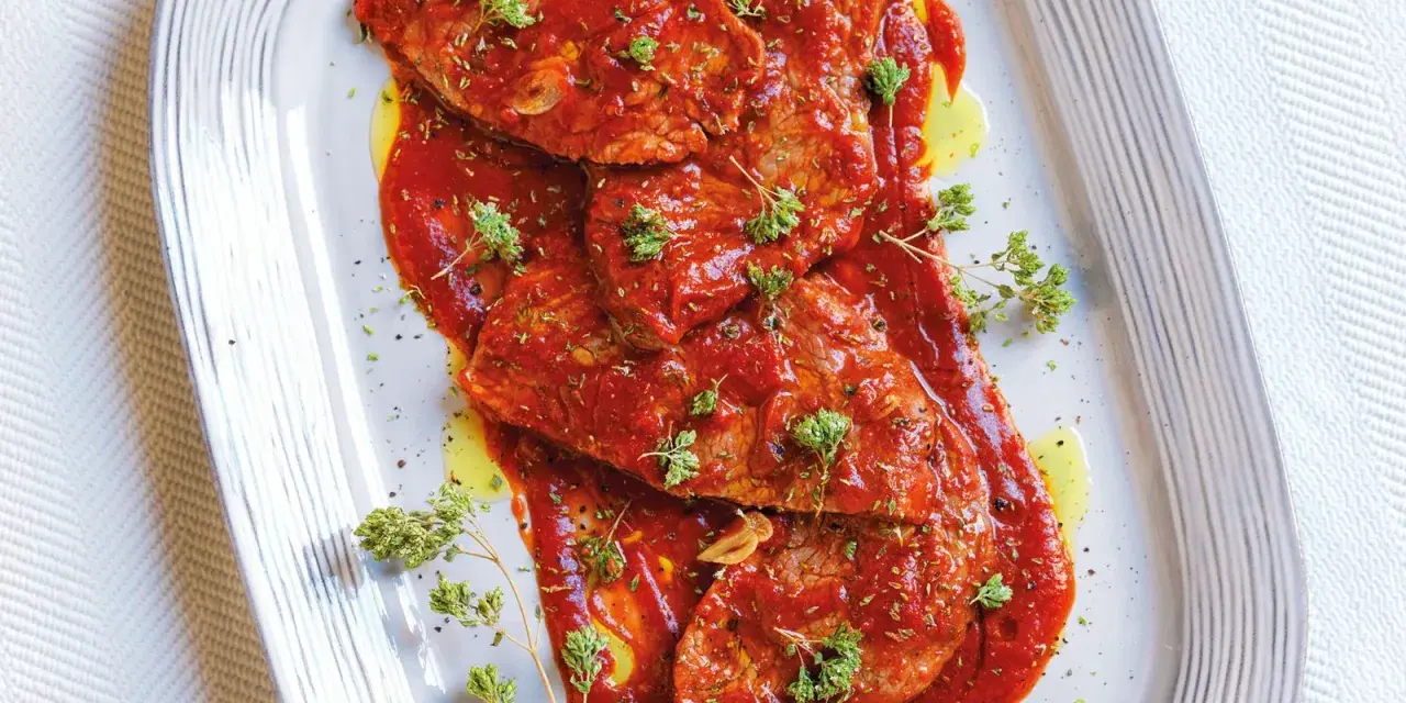 Bistecche alla pizzaiola succulente, ricoperte da salsa rossa e guarnite con erbe aromatiche fresche.