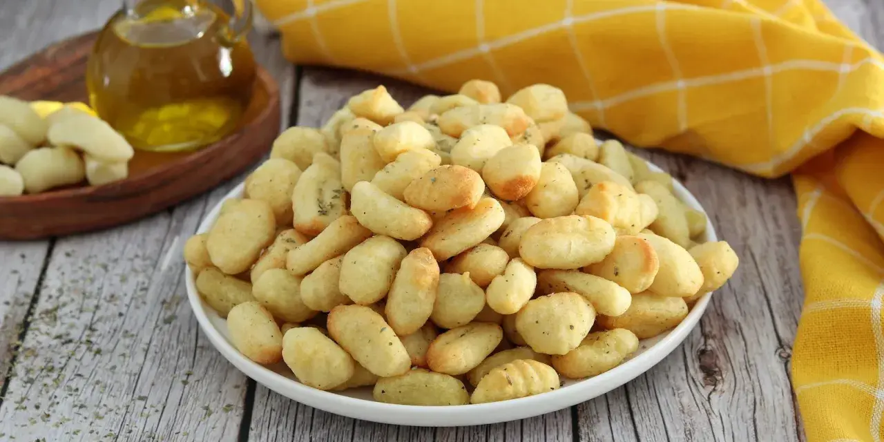 Gnocchi dorati e croccanti, cotti nella friggitrice ad aria, conditi con erbe aromatiche. Accanto, olio d'oliva e gnocchi crudi.