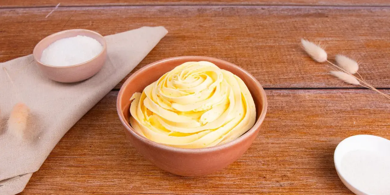 Crema al burro ricetta della nonna, soffice e profumata, pronta per decorare torte. Zucchero e ingredienti in vista.
