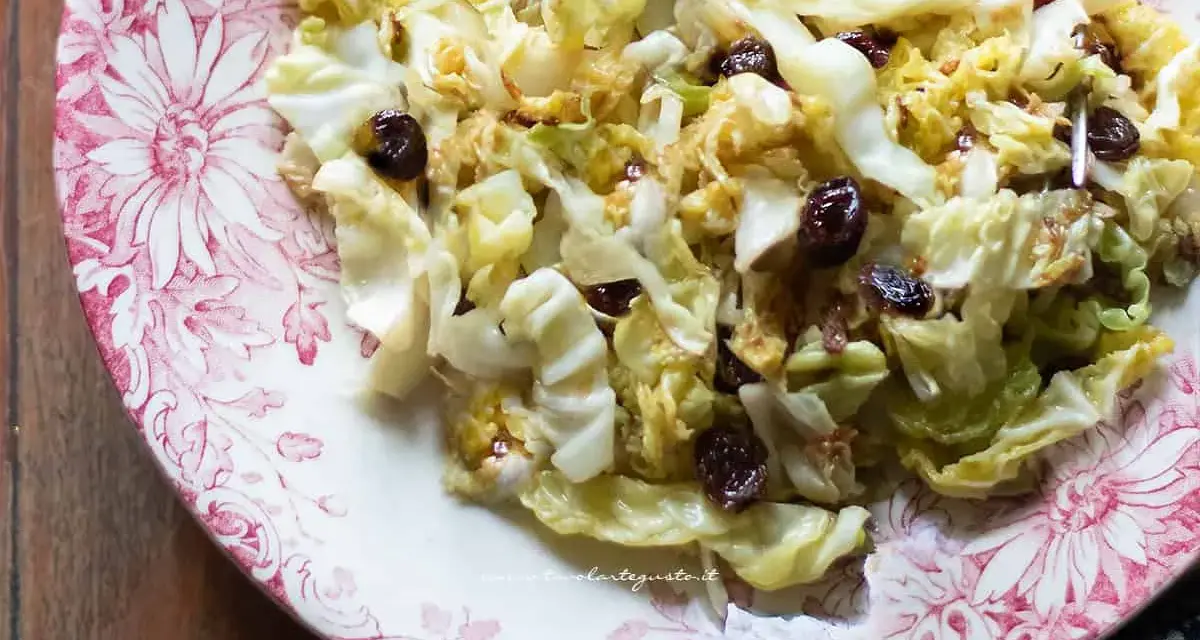 Deliziosa insalata di verza con uvetta, servita su un piatto decorato con fiori rossi.