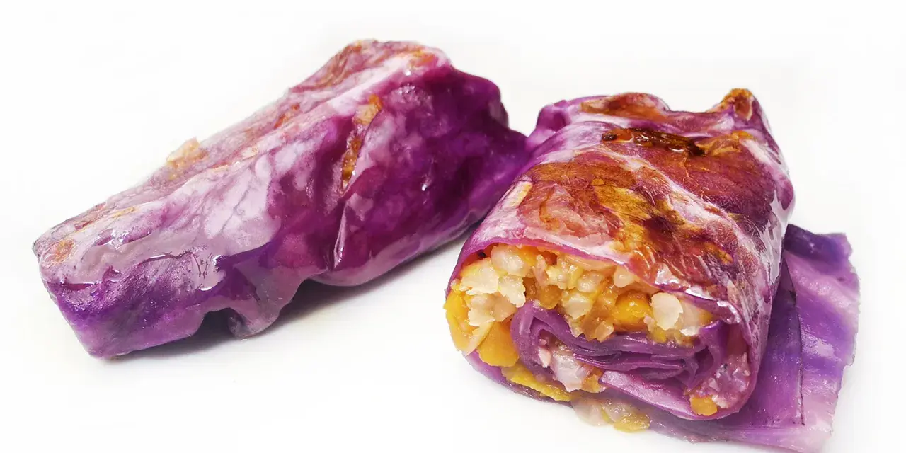 Due involtini di cavolo cappuccio viola, ripieni di riso e verdure, su sfondo bianco.