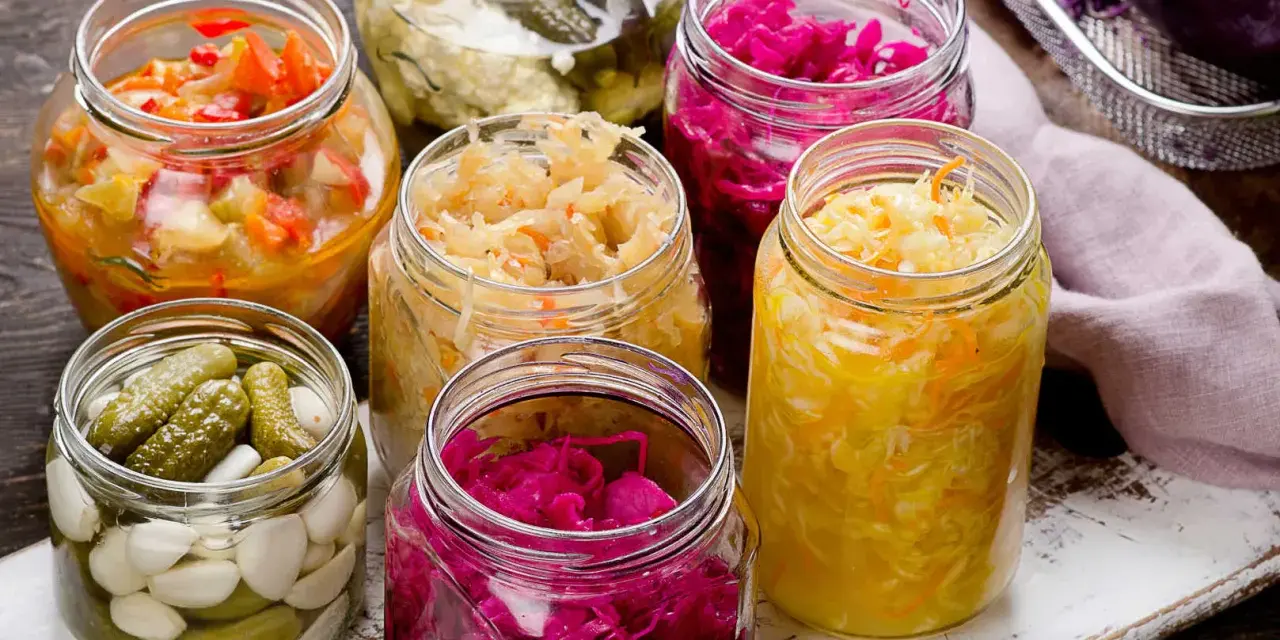 Vasi di vetro pieni di cibi fermentati fatti in casa: crauti, cavolo rosso, cetriolini e verdure miste.