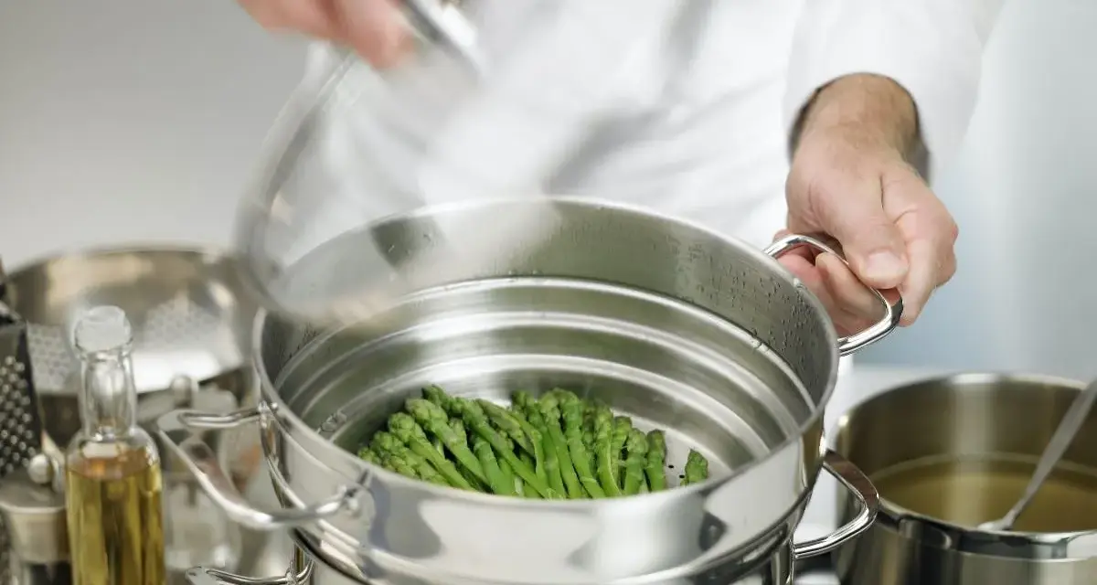 Asparagi freschi pronti per la cottura al vapore in una vaporiera. Un cuoco sta per coprire il cestello.
