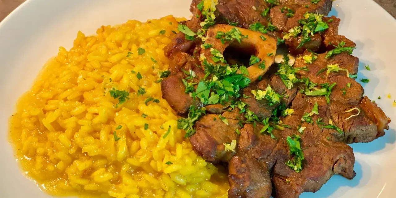 Un piatto invitante di risotto giallo cremoso accanto a un ossobuco tenero, guarnito con prezzemolo fresco e scorza di limone.