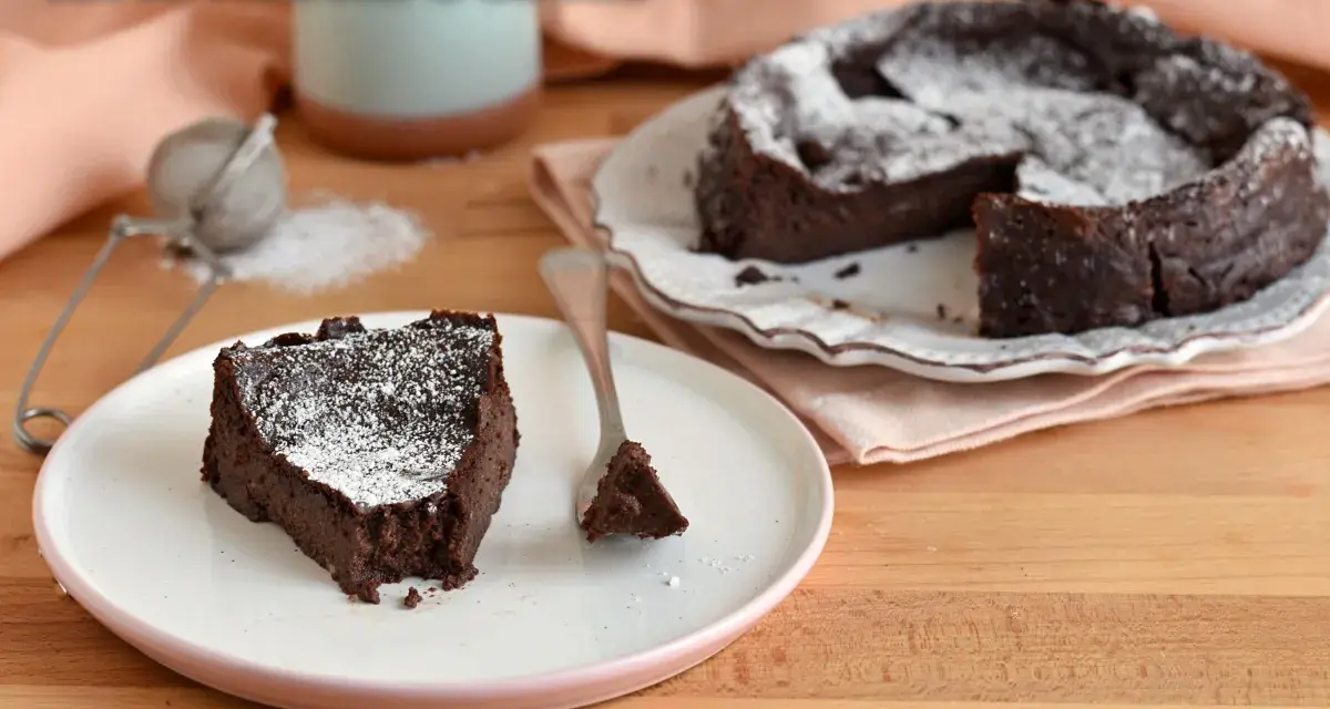 Una fetta di torta ricotta e cioccolato senza farina, cosparsa di zucchero a velo, su un piatto bianco.