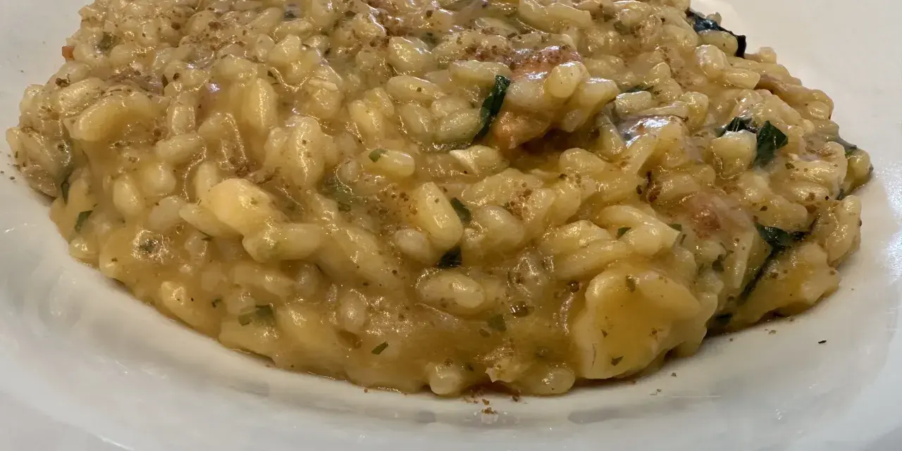 Un cremoso risotto alla pescatora ricetta napoletana, con riso carnaroli e profumi di mare, servito in un piatto bianco.