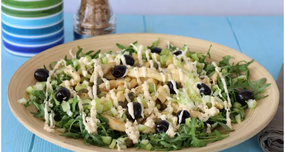 Deliziosa insalata di pollo con rucola, sedano, olive nere e capperi, condita con una cremosa salsa.