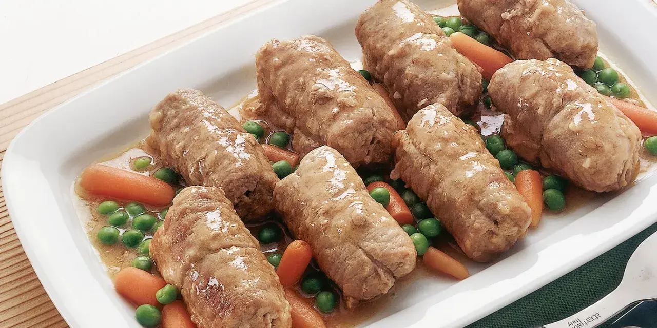 Involtini di carne succulenti serviti con carote e piselli in un piatto bianco.