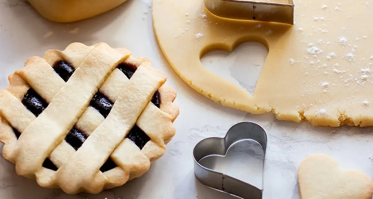 Preparazione di crostatine con pasta frolla classica. Stesa di impasto, formine a cuore e una crostatina già pronta.