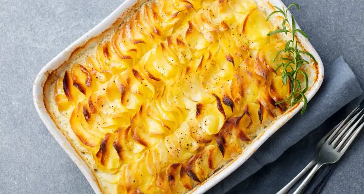 Delizioso millefoglie di patate dorate e croccanti, cotto in una teglia bianca, guarnito con rosmarino fresco e pepe nero.