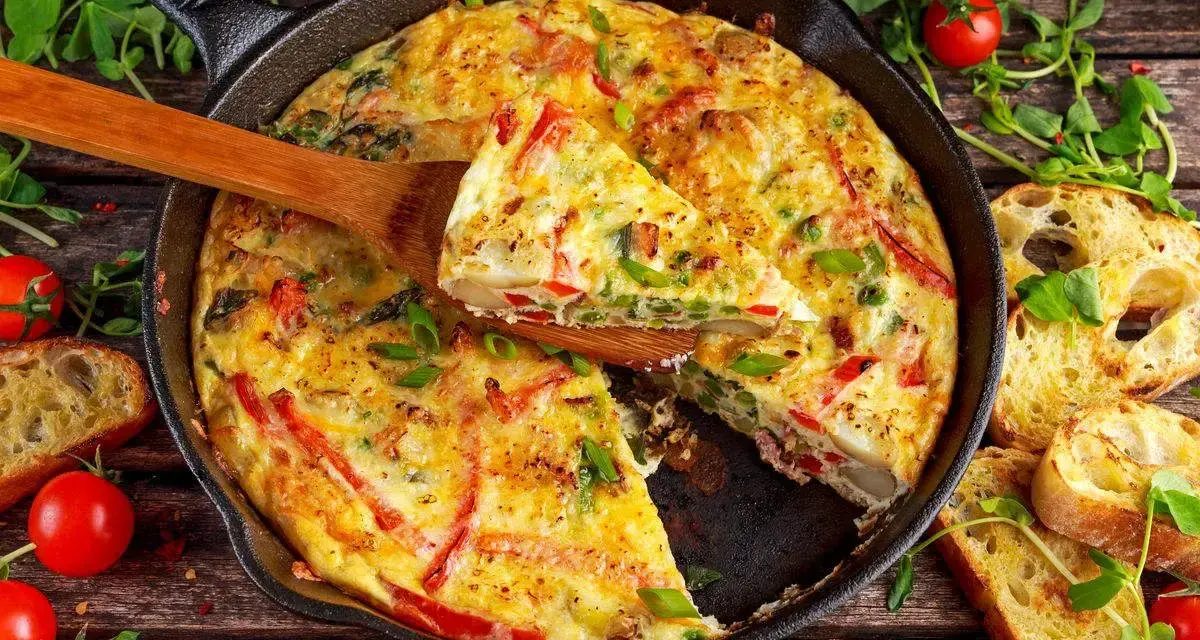 Frittata di peperoni dorata in padella, con fette di pane tostato e pomodorini freschi.