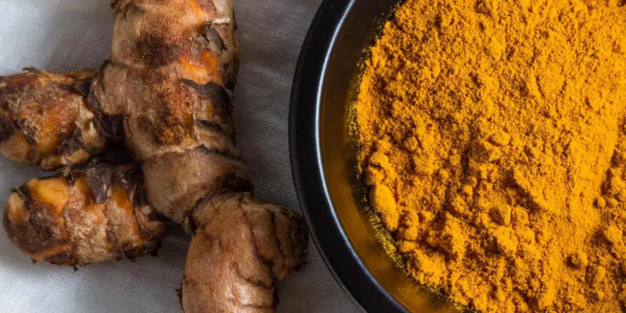 Radici di curcuma e polvere dorata in una ciotola, perfette per dare colore e sapore alla pasta.