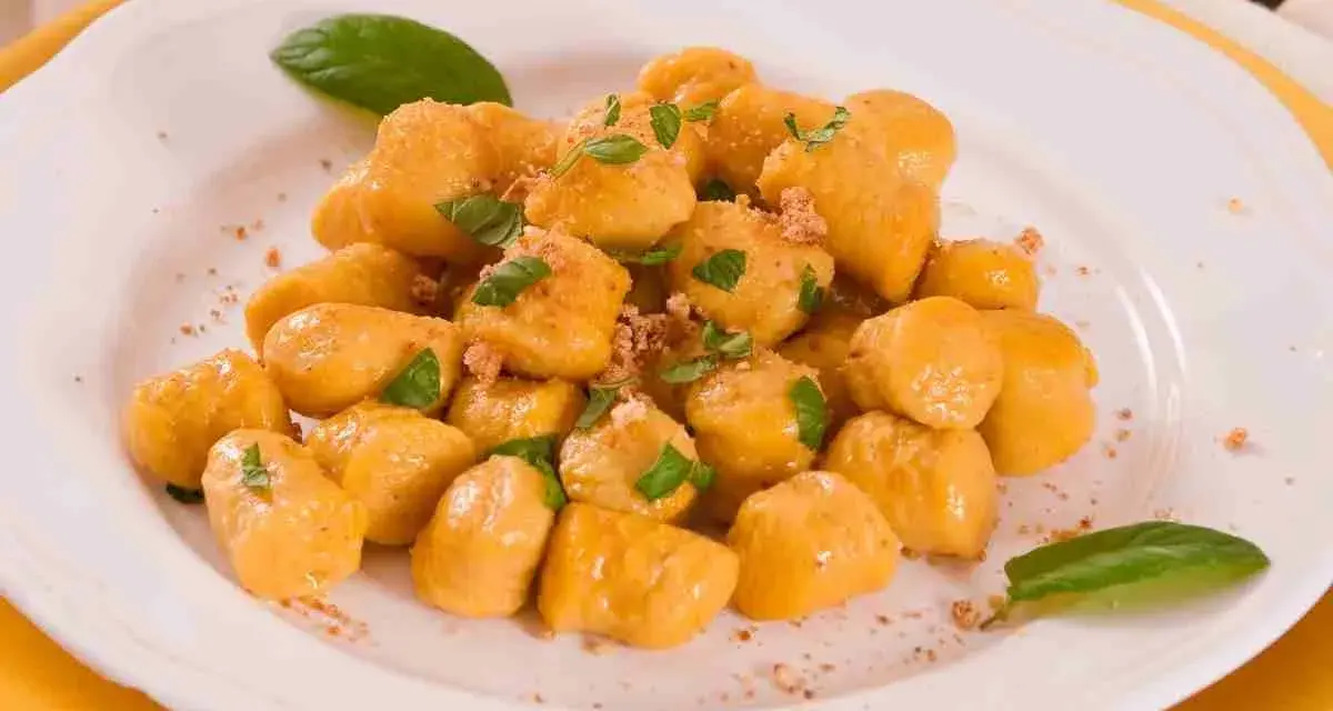 Gnocchi di zucca dorati e soffici, guarniti con basilico fresco e una spolverata di pangrattato croccante, serviti su un piatto bianco.