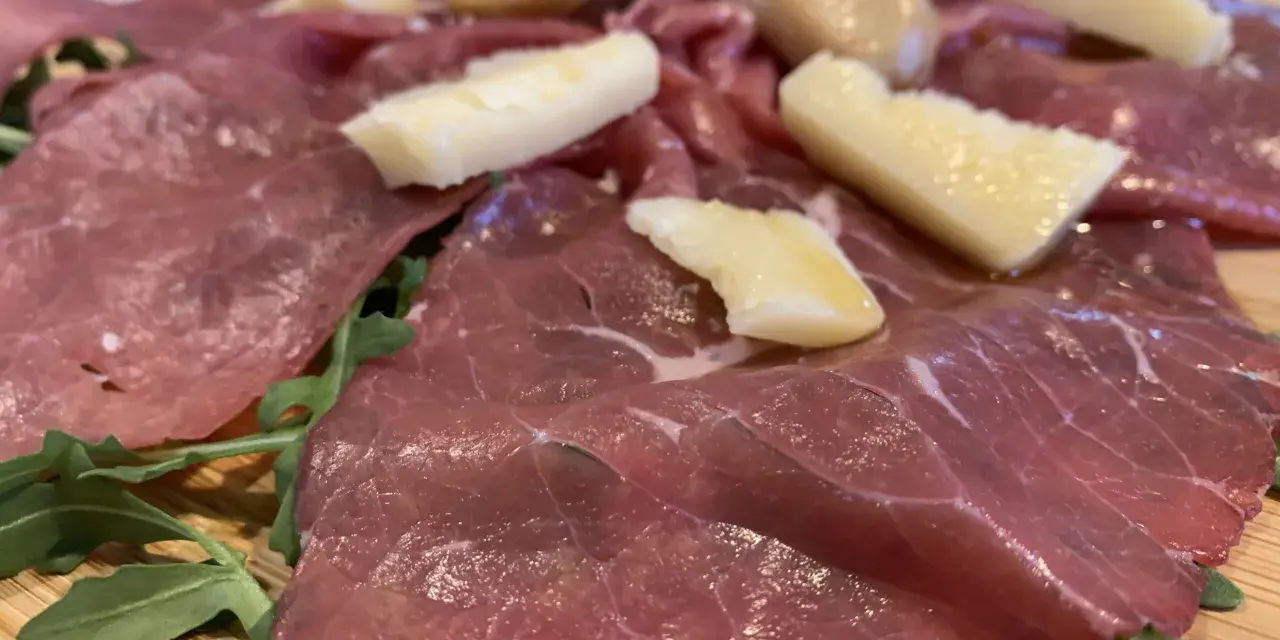 Carne salada cos'è? Fettine sottili di carne rossa, condite con erbe aromatiche e scaglie di formaggio stagionato, su un letto di rucola fresca.