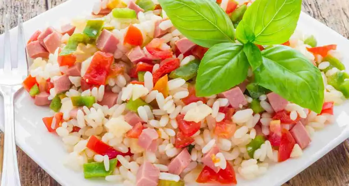 Un colorato insalata di riso con cubetti di prosciutto, peperoni e pomodori, guarnita con foglie di basilico fresco.