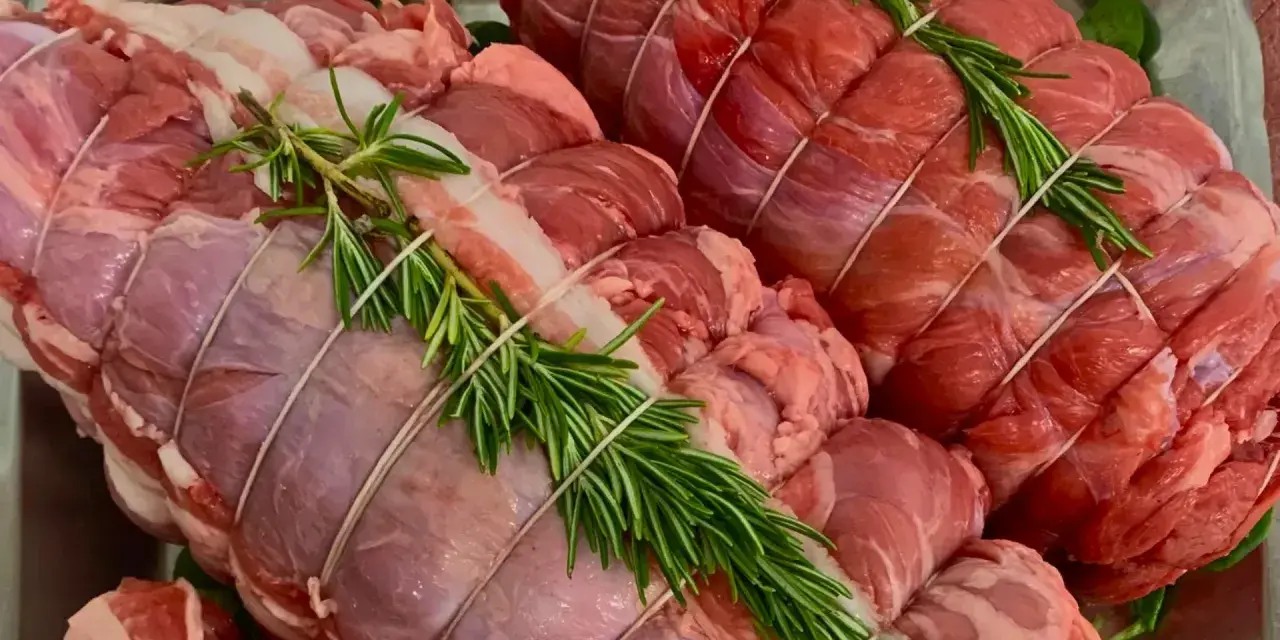 Due **tagli di carne per arrosto** pronti per essere cucinati, legati con spago e guarniti con rametti di rosmarino fresco.