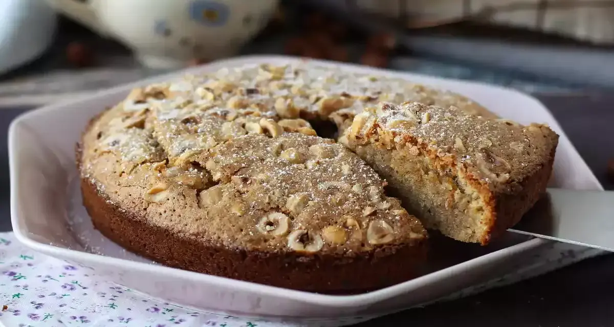 Deliziosa torta di nocciole senza farina, cosparsa di zucchero a velo e nocciole intere. Perfetta per ogni occasione.