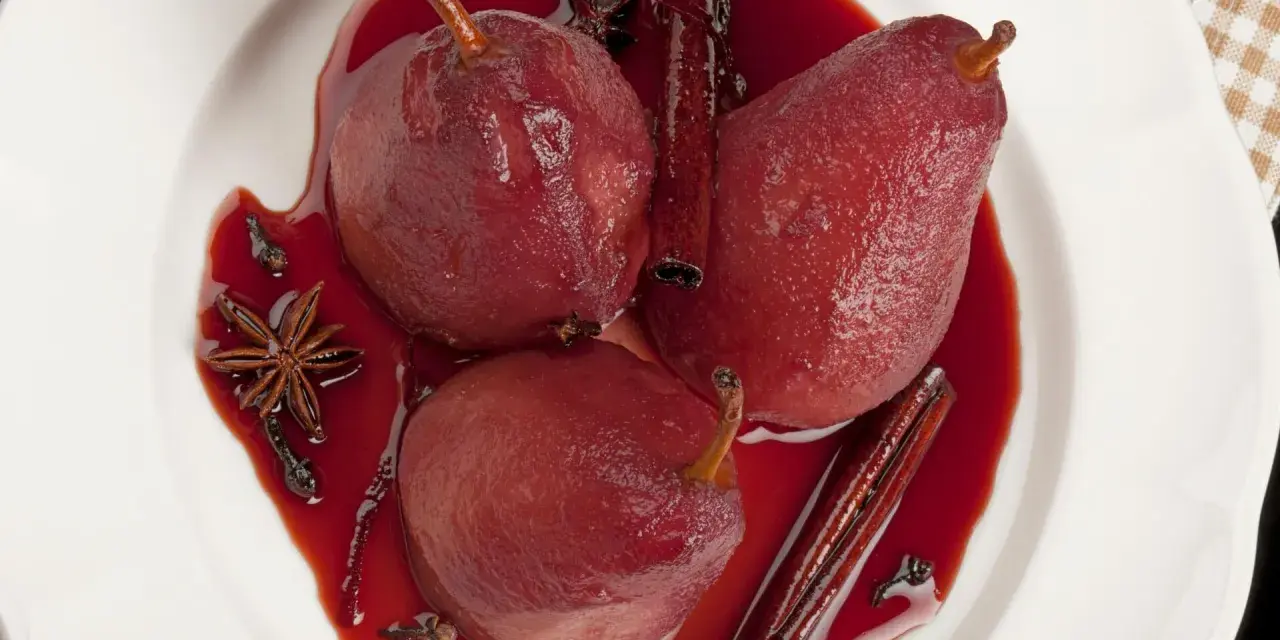 Pere cotte nel vino, profumate con cannella, anice stellato e chiodi di garofano, servite in una ciotola bianca.