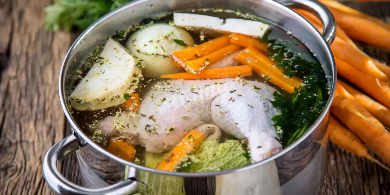 Brodo di pollo in pentola a pressione con carote, cipolla, sedano e prezzemolo.