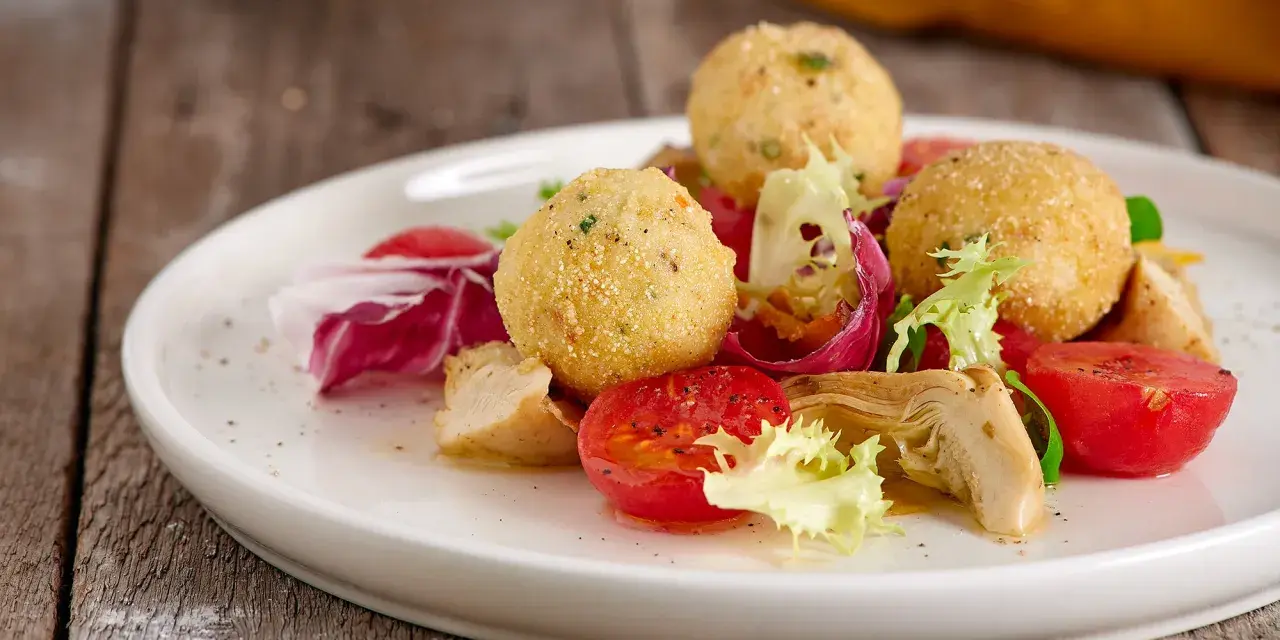 Sfere dorate di miglio fritte, servite con un'insalata fresca di pomodorini, radicchio e pollo. Un'idea gustosa per le tue ricette con miglio.