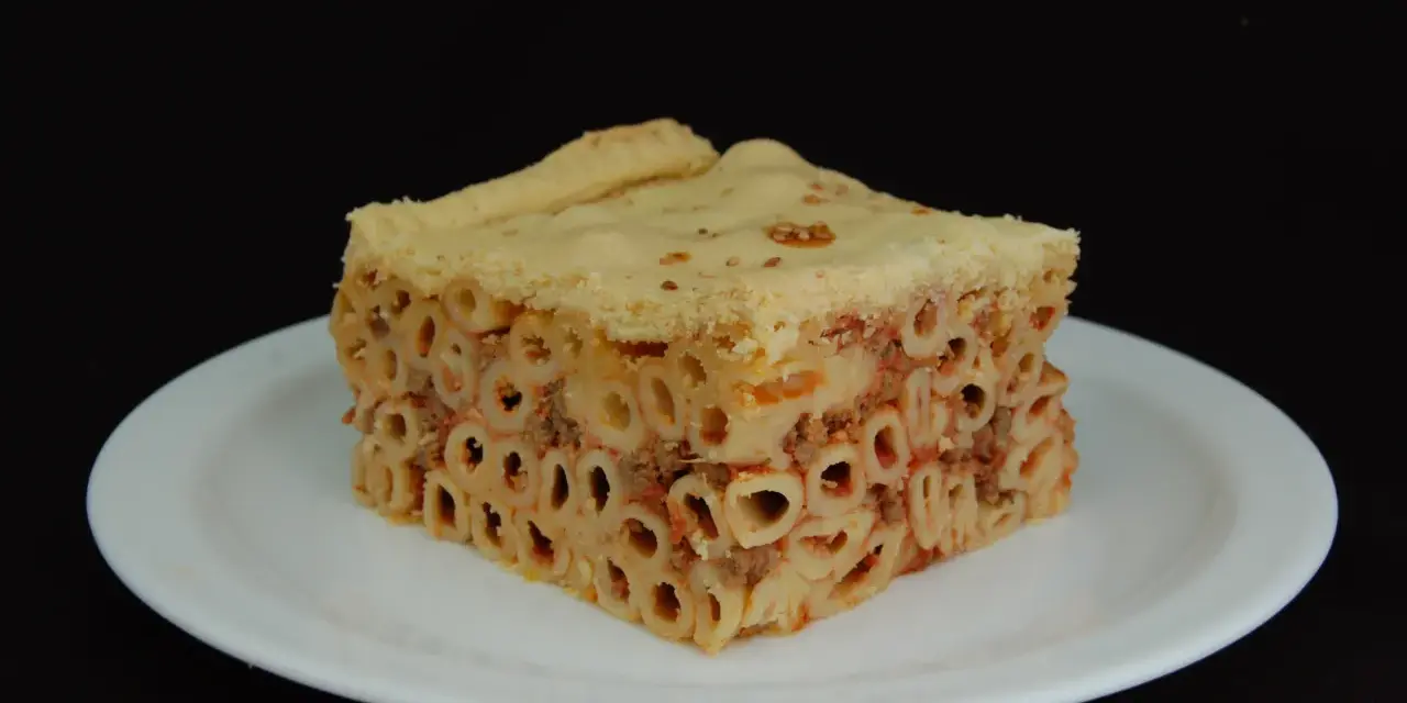 Un pezzo di timballo di pasta con ragù e pasta cotta al forno, servito su un piatto bianco.