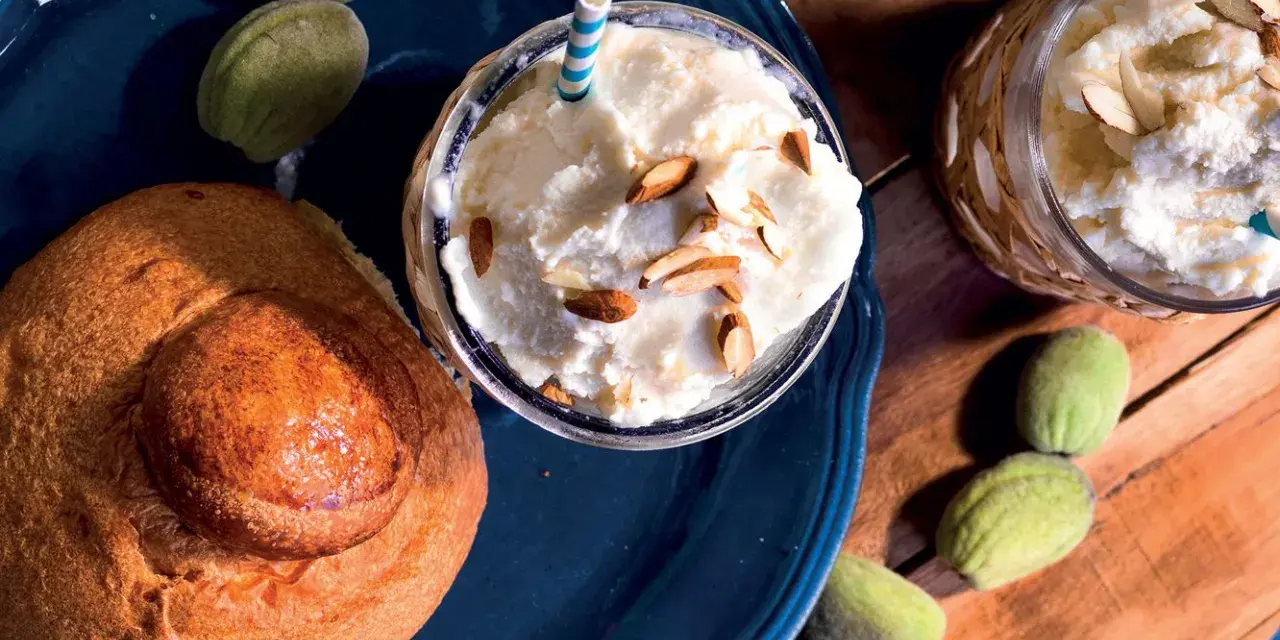 Deliziosa granita di mandorle servita con mandorle a lamelle e pane dolce. Freschezza siciliana in un bicchiere.