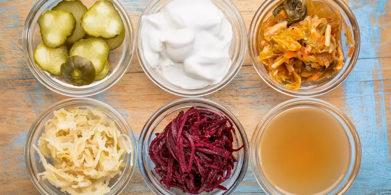 Sei ciotole di vetro con cetrioli, yogurt, kimchi, crauti, barbabietole e brodo, ingredienti per probiotici naturali fatti in casa.