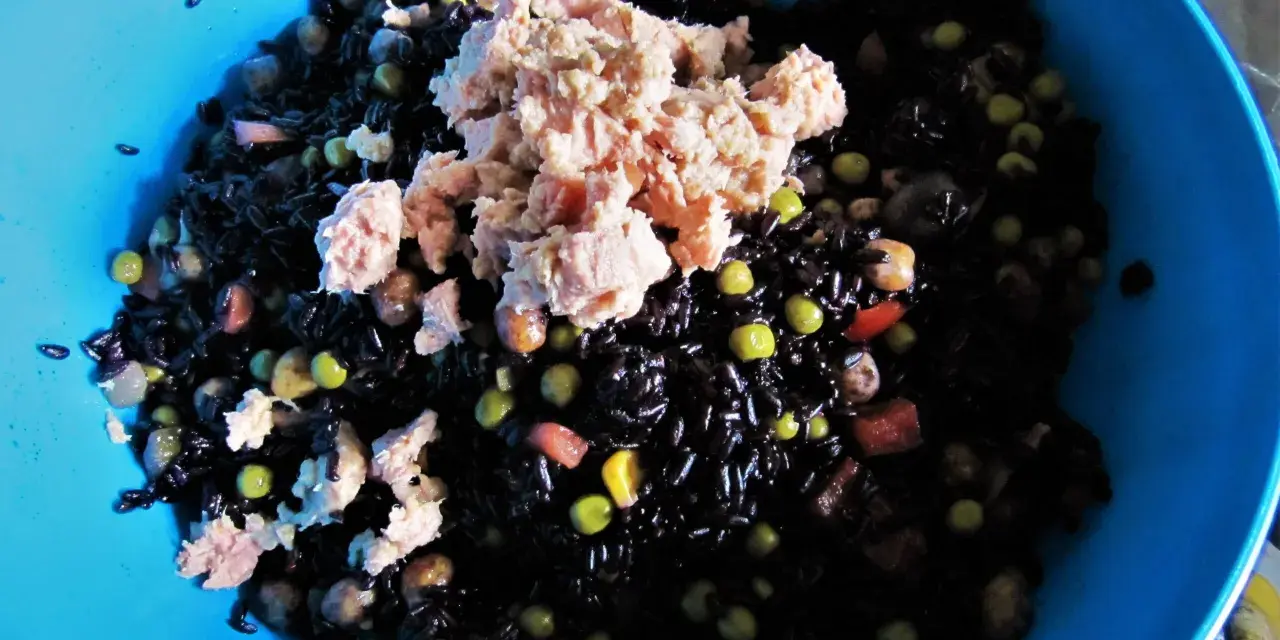 Un'insalata di riso nero con tonno, piselli e cubetti di pomodoro. La cottura del riso nero è perfetta, ogni chicco è ben separato.