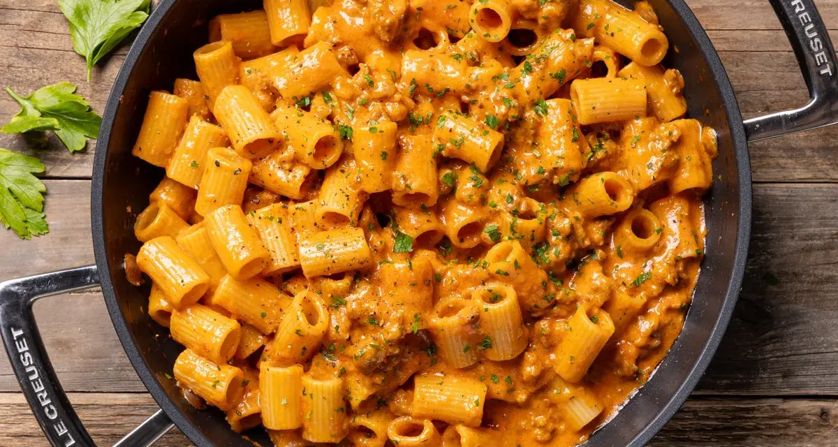 Un invitante piatto di pasta con salsiccia alla napoletana, condita con una cremosa salsa arancione e prezzemolo fresco.