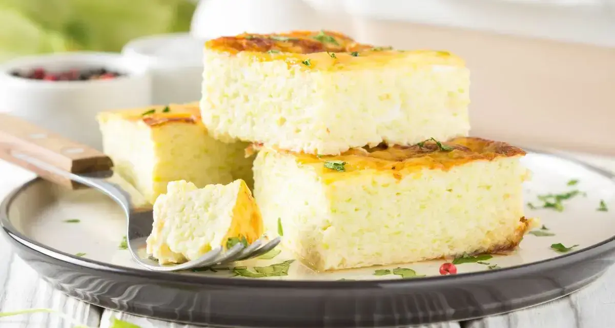 Fetta di frittata al forno soffice e alta, guarnita con erbe aromatiche, su un piatto scuro.