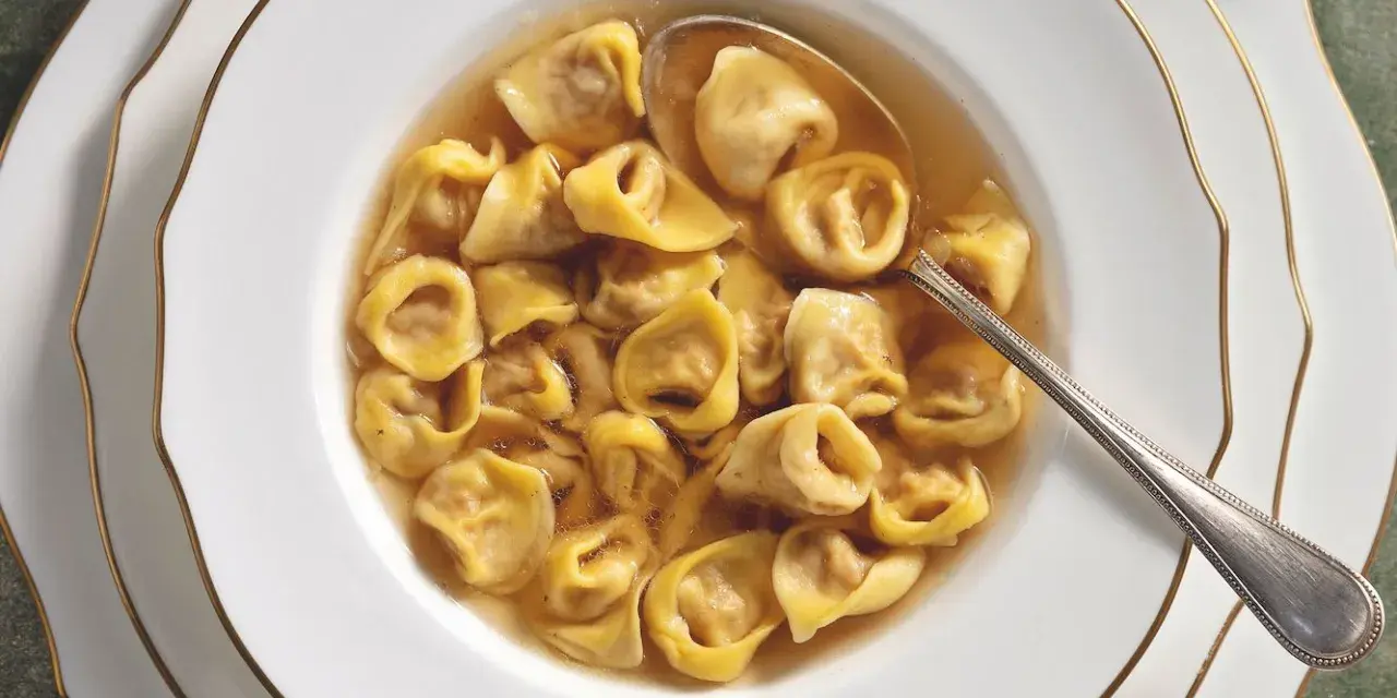Un primo piatto fumante: tortellini in brodo, un classico della tradizione culinaria italiana, serviti in una ciotola bianca con bordo dorato.