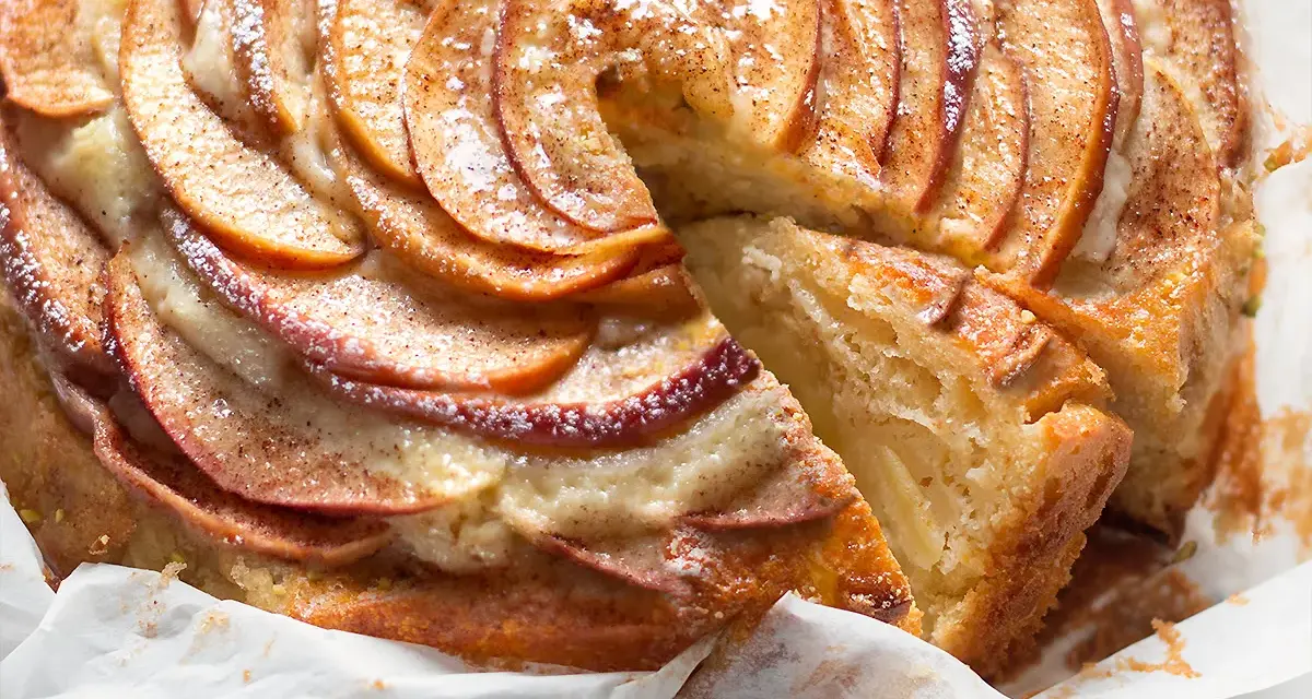Una fetta di torta di mele e yogurt soffice, con mele a spirale e spolverata di cannella.