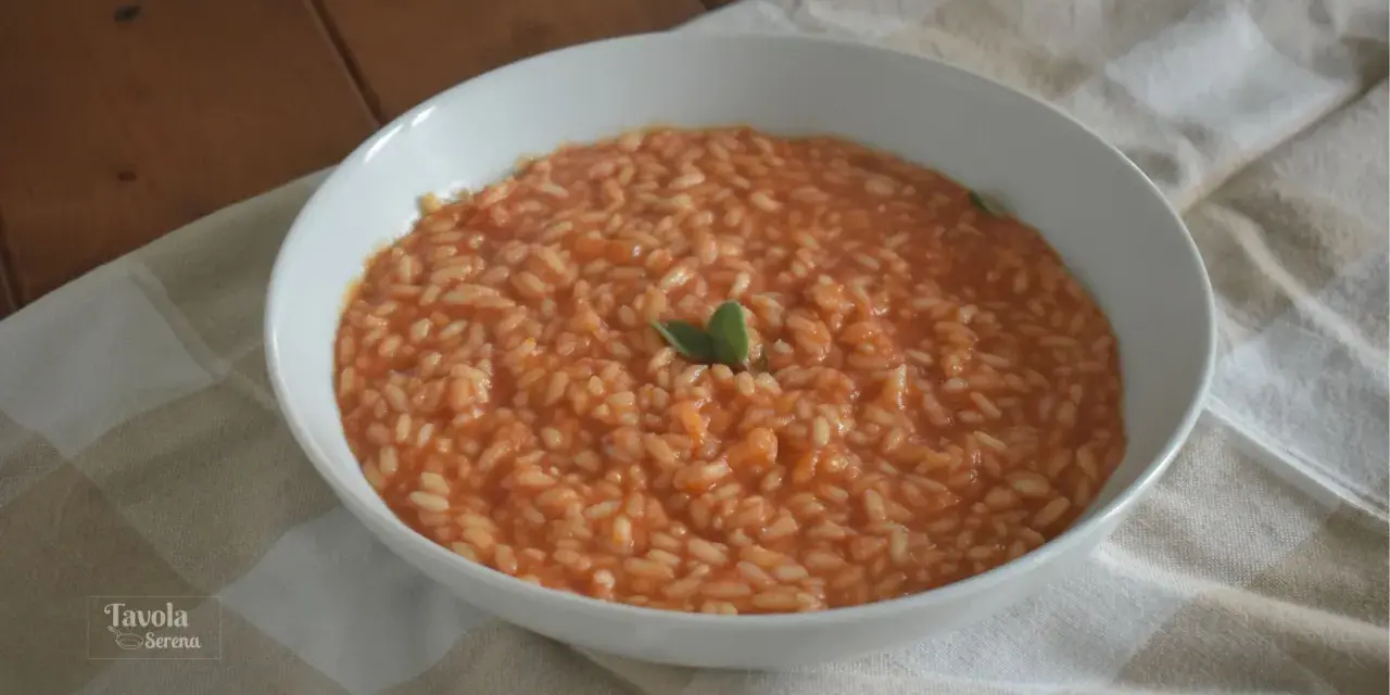 Un cremoso riso al pomodoro veloce, guarnito con una fogliolina verde, servito in una ciotola bianca su una tovaglia a quadri.