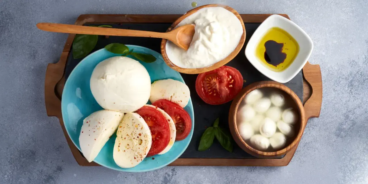 La differenza tra burrata e mozzarella è evidente: la burrata cremosa in ciotola, la mozzarella fresca su piatto con pomodoro.