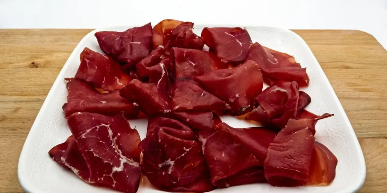 Fette di bresaola, la bresaola che carne è, su un piatto bianco.