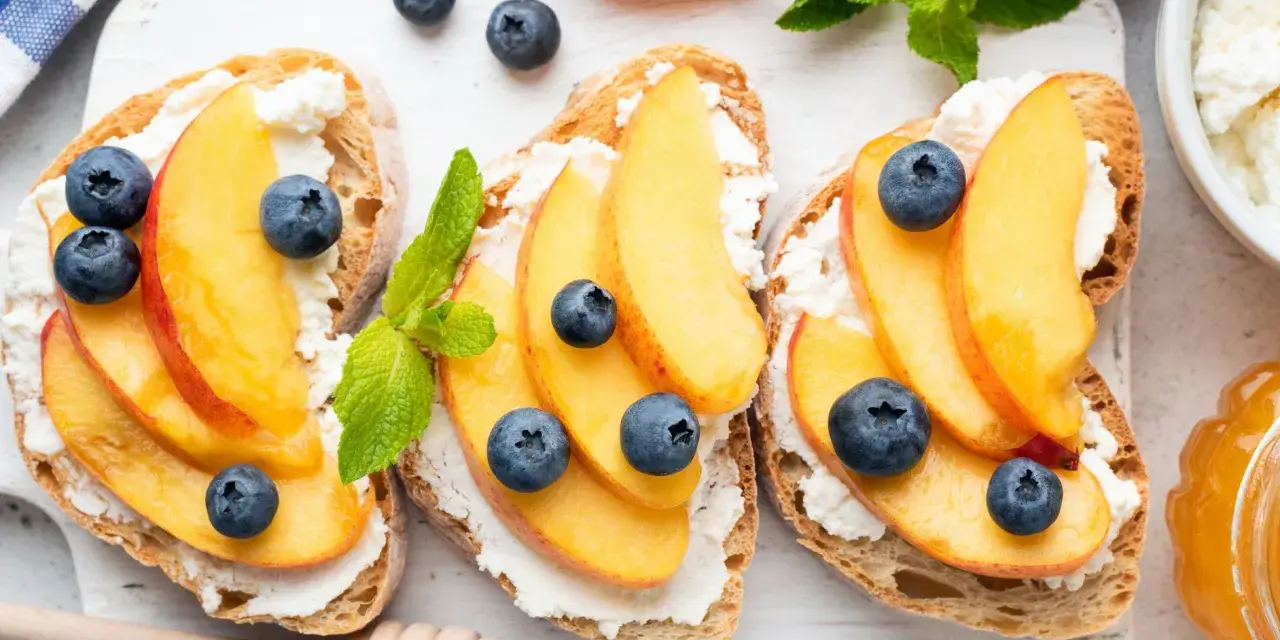 Bruschette con pesche mature, ricotta e mirtilli. Un'idea fresca per ricette con pesche mature, perfetta per la colazione o uno spuntino leggero.