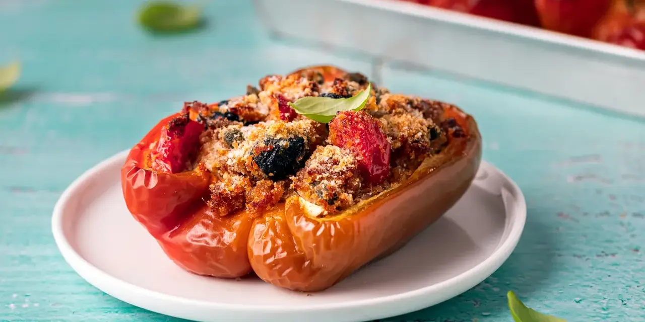 Peperoni ripieni, un classico delle ricette con peperoni, con un gustoso ripieno di pomodoro, olive e pangrattato, guarniti con basilico fresco.