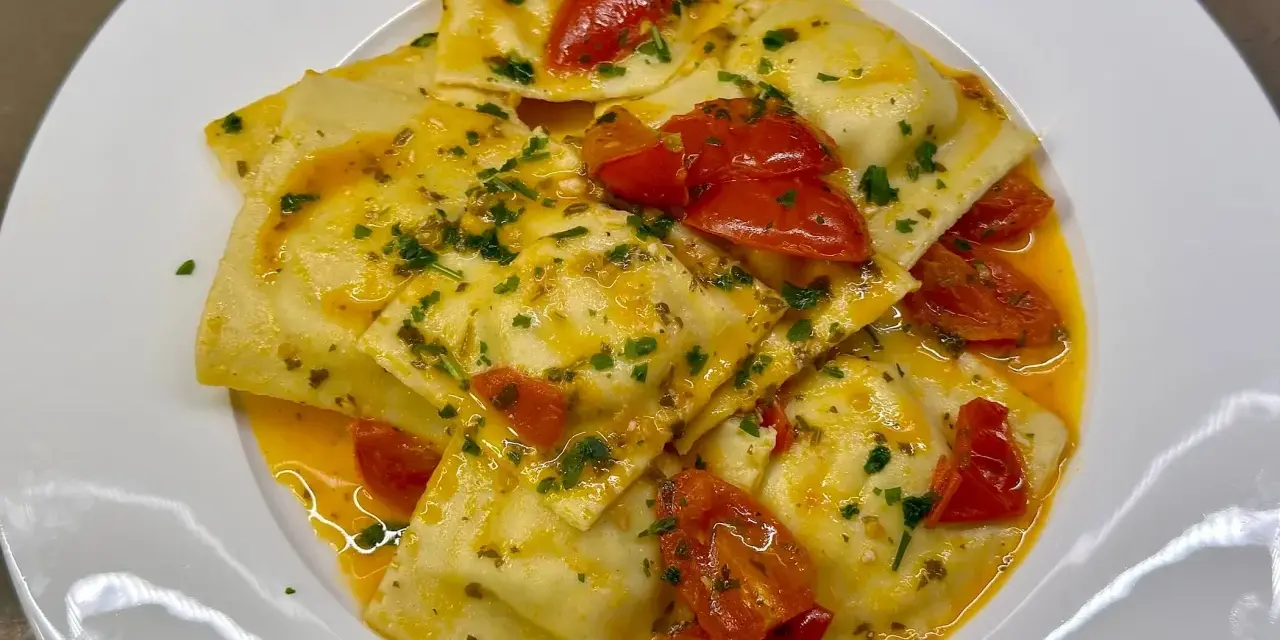 Deliziosi ravioli di pesce conditi con pomodorini e prezzemolo, in un sugo dorato.