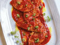 Bistecche alla pizzaiola succulente, ricoperte da salsa rossa e guarnite con erbe aromatiche fresche.