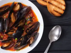 Un invitante piatto di zuppa di cozze in salsa rossa, accompagnato da crostini tostati e un cucchiaio d'argento.