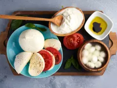 La differenza tra burrata e mozzarella è evidente: la burrata cremosa in ciotola, la mozzarella fresca su piatto con pomodoro.