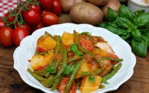 Un piatto di fagiolini e patate alla pugliese, con pomodorini freschi e basilico, pronto per essere gustato.