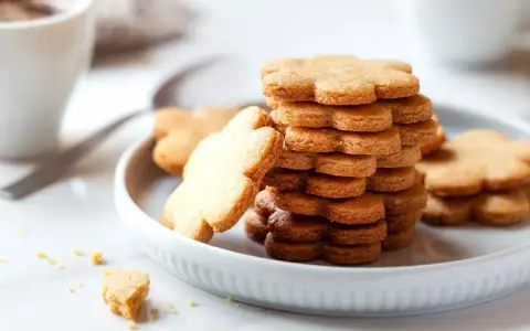Una pila di biscotti pasta frolla a forma di fiore su un piatto bianco, con una tazza di caffè sullo sfondo.