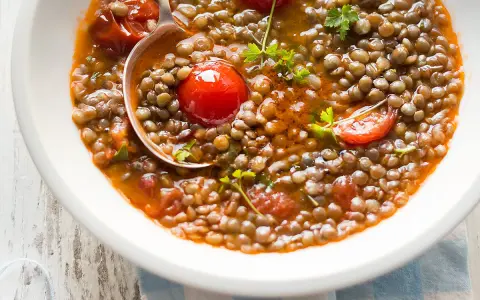 Una ciotola di zuppa di lenticchie veloce con pomodorini e prezzemolo fresco. Un cucchiaio serve la gustosa zuppa.