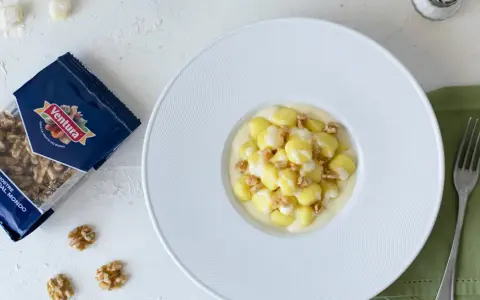 Gnocchi al Castelmagno con noci croccanti, un piatto cremoso e saporito. La confezione di noci Ventura accanto promette un tocco di gusto in più.