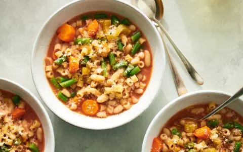 Tre ciotole di fumante pasta e fagioli vegetariana, ricca di verdure e condita con parmigiano.