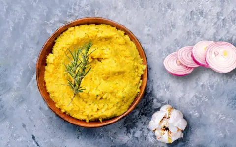 Piatto di lenticchie decorticate cremose, guarnito con rosmarino, cipolla rossa affettata e aglio.